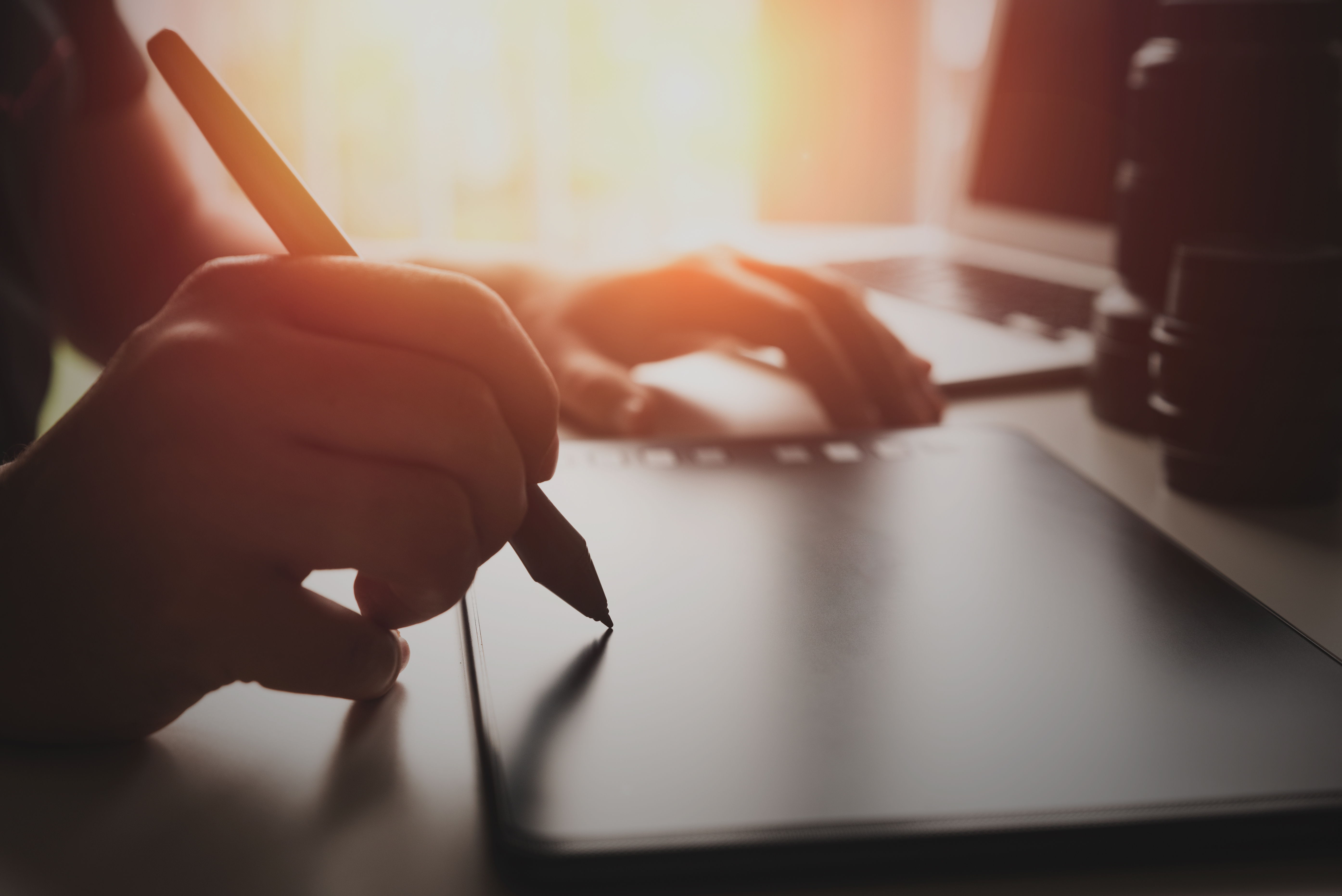 One hand is holding a digital pen to create a design on a tablet while the other is resting on the side