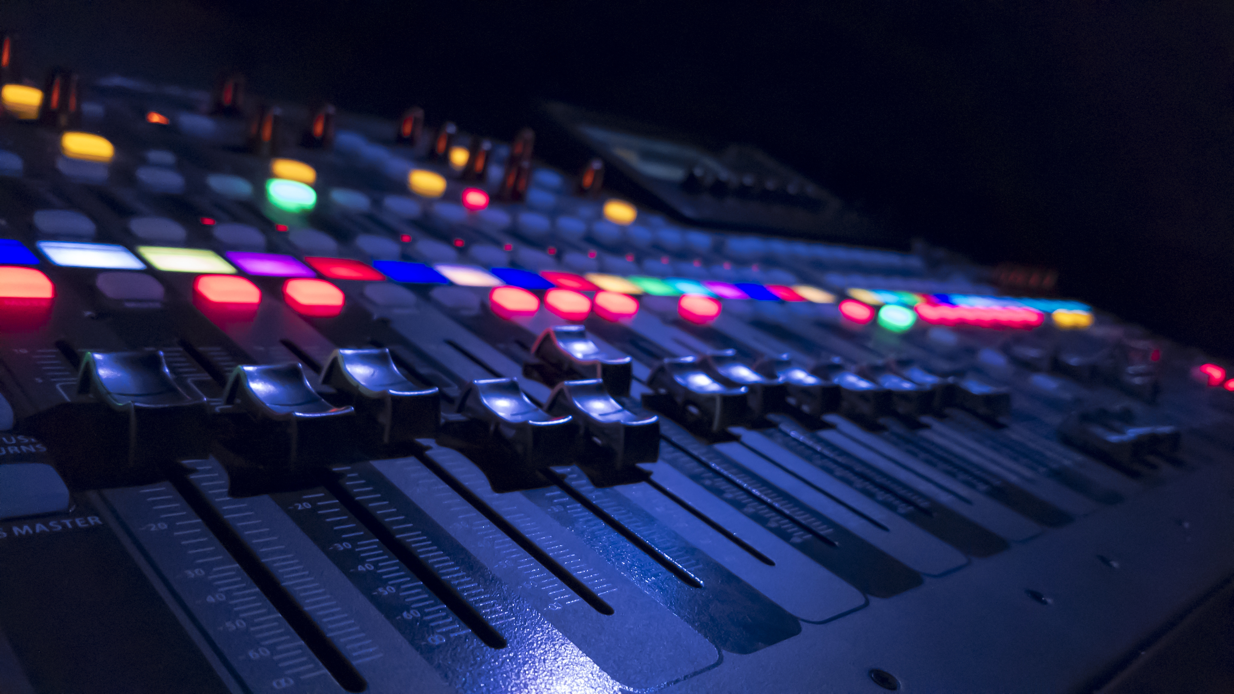 A colorful mixing console in a dark room lit up with bright colors