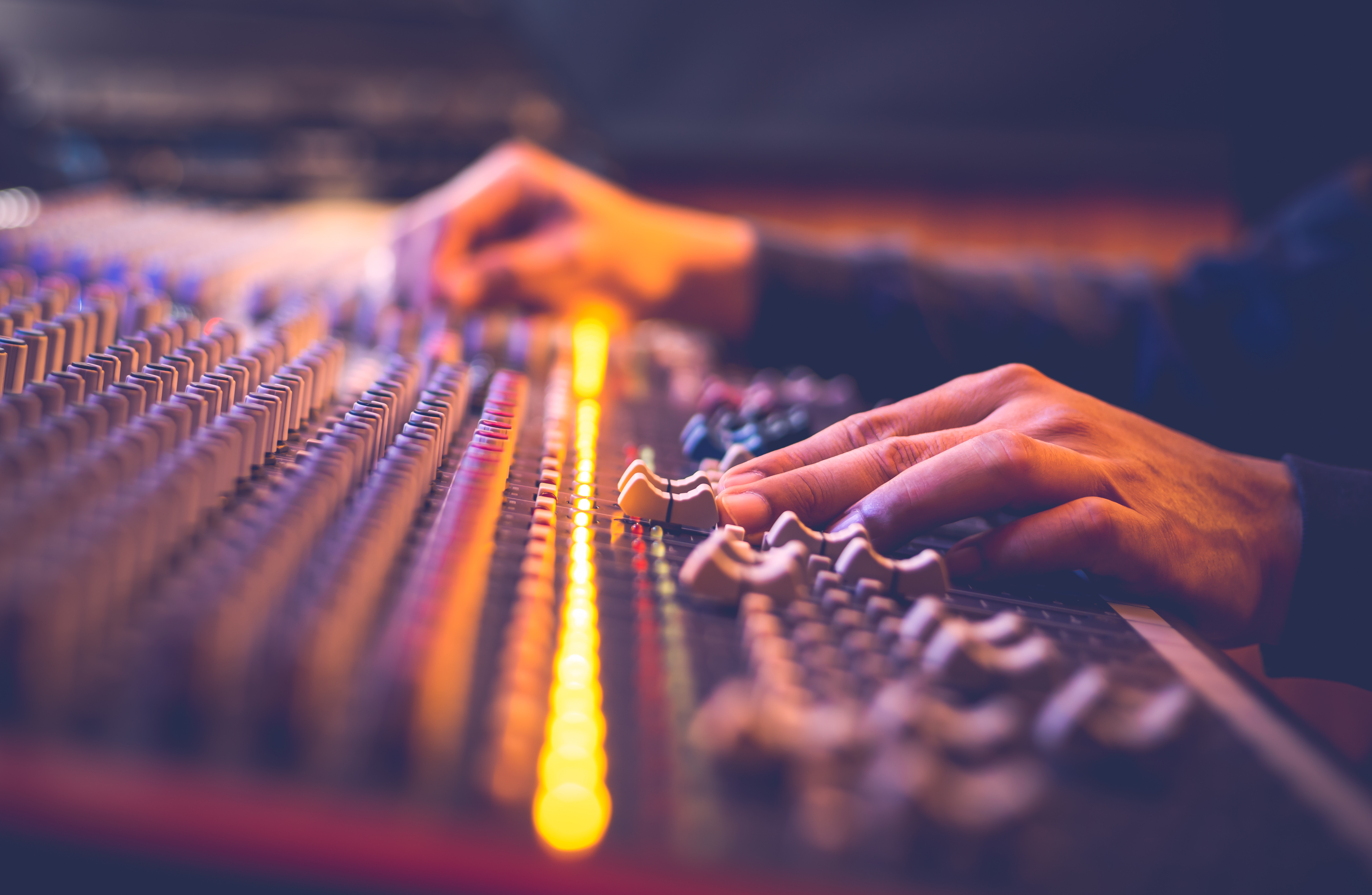 Two hands on a mixing console, sliding levers around during production.